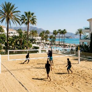 Campo da beach volley in un lussuoso resort spagnolo con figure in lontananza che giocano. (Immagine generata con IA)