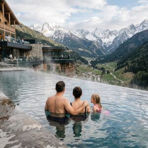 Famiglia vista di spalle che si rilassa in una piscina esterna riscaldata di un resort alpino, con vista su montagne innevate.