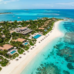 Vista aerea di un lussuoso resort su una spiaggia di Turks e Caicos con ville private, un ristorante panoramico e persone che fanno snorkeling.