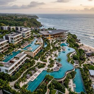 Vista aerea di un lussuoso resort moderno con piscine, giardini tropicali e architettura elegante, che si estende verso il mare.