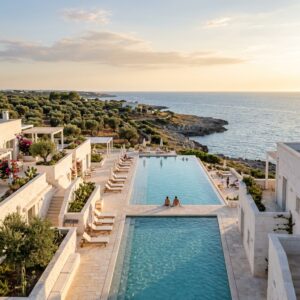 Piscina a sfioro di un lussuoso resort dal design moderno e bianco, con ulivi e vista sul mare Adriatico al tramonto in Puglia.