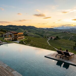 Piscina a sfioro di un resort di lusso con vista sui vigneti delle Langhe, con una coppia in lontananza.